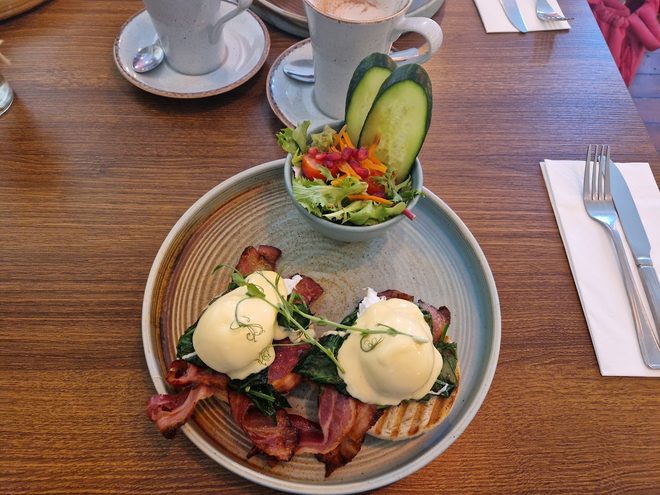 Eggs Benedict with bacon on a dark wooden table with coffee behind